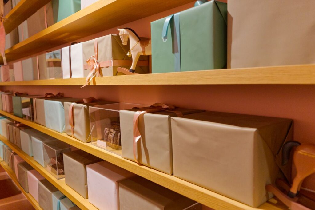Shelves filled with neatly wrapped gift boxes in pastel colors, organized with ribbons and clear storage containers. 